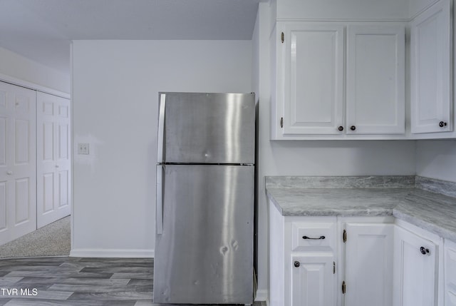 kitchen with freestanding refrigerator, white cabinetry, light countertops, and wood finished floors