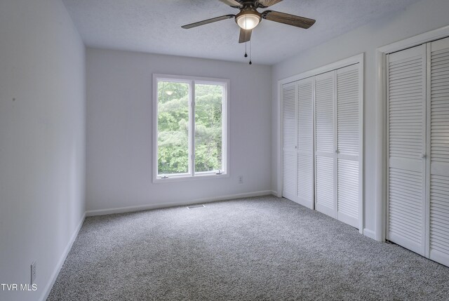 unfurnished bedroom featuring carpet, baseboards, two closets, ceiling fan, and a textured ceiling