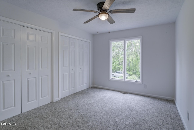 unfurnished bedroom featuring carpet floors, multiple closets, baseboards, and a textured ceiling
