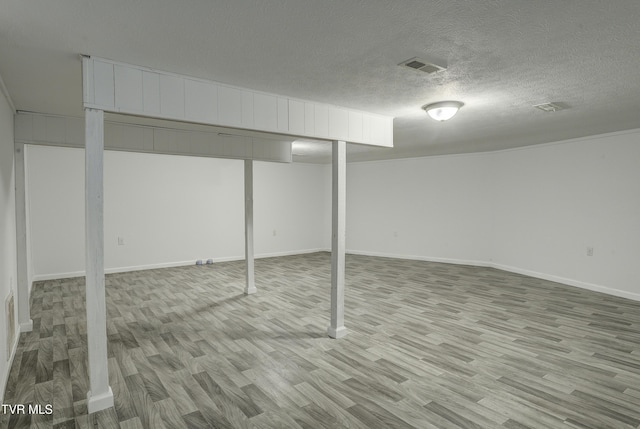 finished below grade area featuring light wood finished floors, baseboards, and a textured ceiling