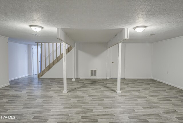 finished below grade area with wood finished floors, a textured ceiling, stairway, and baseboards