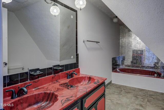 bathroom featuring a textured ceiling, a bath, double vanity, toilet, and lofted ceiling