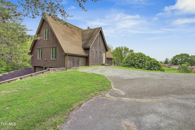 view of side of property featuring roof with shingles, a chimney, a lawn, driveway, and a garage