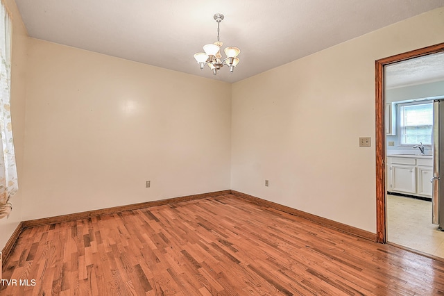 spare room featuring a sink, baseboards, light wood-style flooring, and a chandelier