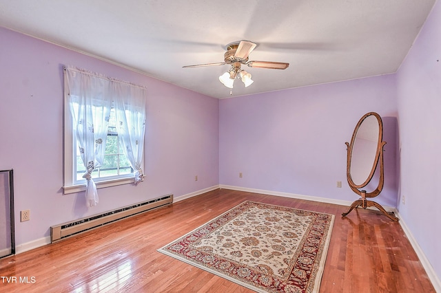 spare room featuring a ceiling fan, baseboards, a baseboard heating unit, and wood finished floors