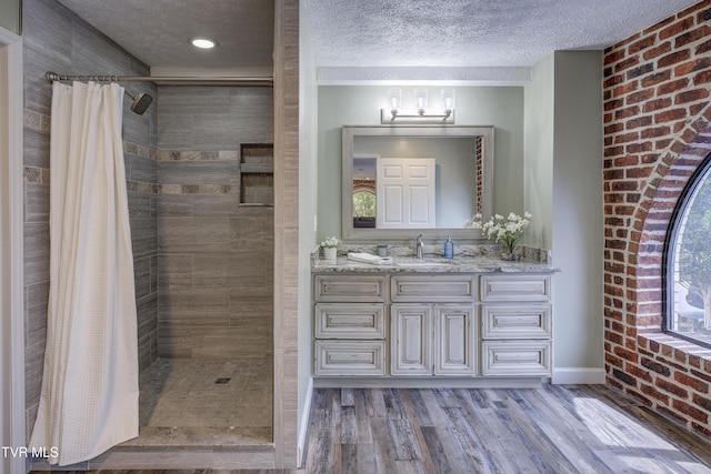 200 E Main St Unit 201, Johnson City, TN 37604 - bathroom with tiled shower, vanity, a textured ceiling, wood finished floors, and brick wall