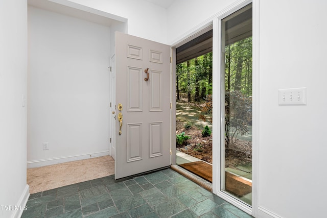 entryway with baseboards and dark colored carpet