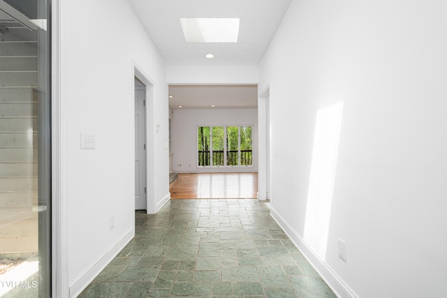 hallway featuring stone tile flooring, recessed lighting, baseboards, and a skylight