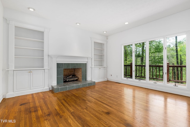 unfurnished living room with baseboards, wood finished floors, a tiled fireplace, and built in shelves