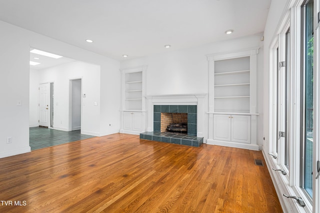 unfurnished living room featuring visible vents, built in features, wood finished floors, baseboards, and recessed lighting