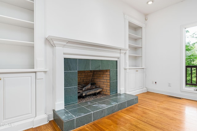 room details featuring built in features, baseboards, wood finished floors, a tile fireplace, and visible vents