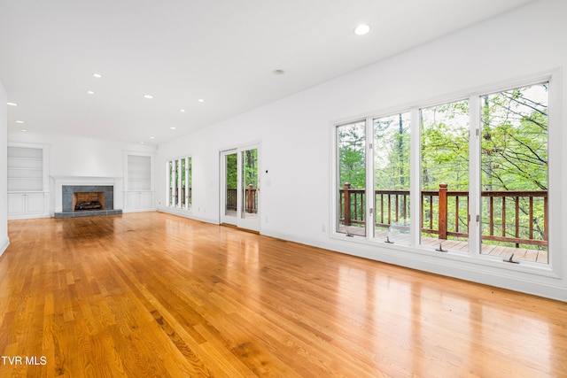 unfurnished living room featuring recessed lighting, light wood-type flooring, built in shelves, and a fireplace