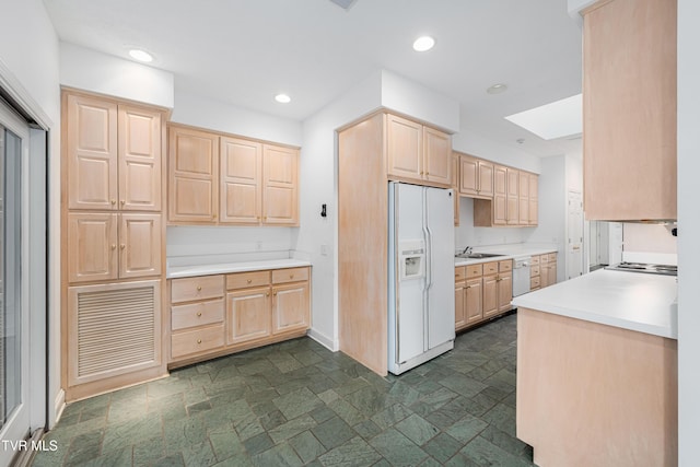kitchen featuring a skylight, light brown cabinetry, stone finish floor, and white appliances