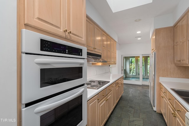 kitchen featuring a skylight, light countertops, under cabinet range hood, recessed lighting, and white appliances
