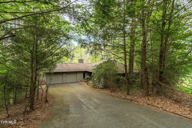 view of front of house featuring a garage, a chimney, and aphalt driveway