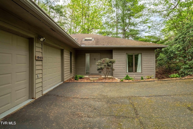 view of exterior entry featuring aphalt driveway, a shingled roof, and a garage
