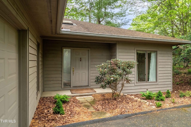 view of exterior entry with roof with shingles and a garage