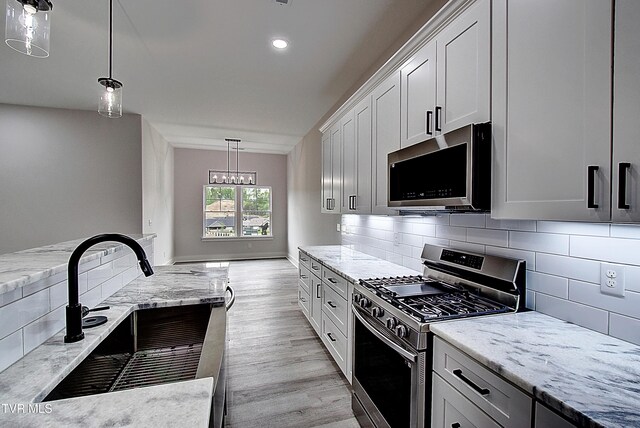 kitchen with decorative backsplash, appliances with stainless steel finishes, a sink, light stone counters, and light wood-style floors