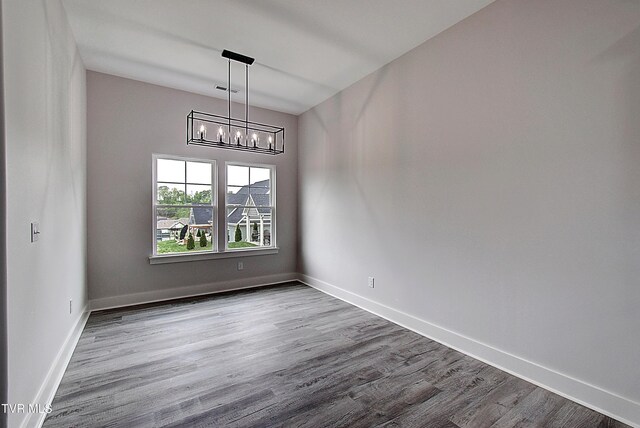 unfurnished dining area with baseboards, visible vents, wood finished floors, and a notable chandelier