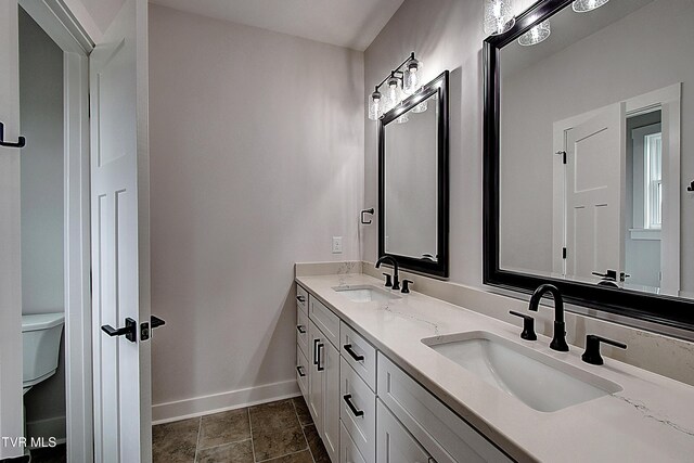 full bathroom with a sink, baseboards, toilet, and double vanity
