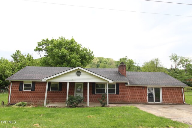 single story home featuring brick siding, a front yard, a chimney, and covered porch