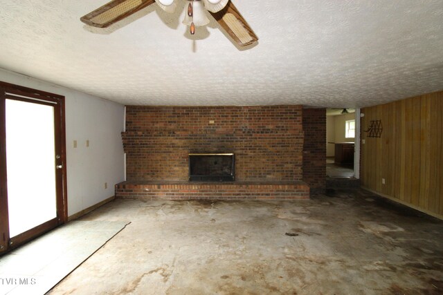 unfurnished living room featuring a brick fireplace, a textured ceiling, concrete floors, a ceiling fan, and baseboards