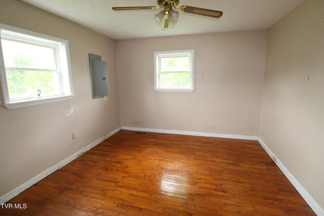 empty room featuring a ceiling fan, baseboards, wood finished floors, and electric panel