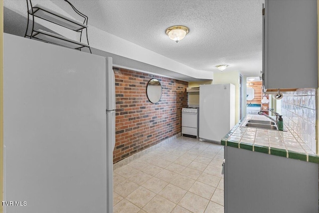 196 Furches Dr, Gray, TN 37615 - kitchen with white appliances, tile counters, a sink, brick wall, and a textured ceiling