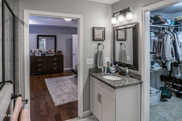 bathroom featuring a walk in closet, wood finished floors, baseboards, and vanity