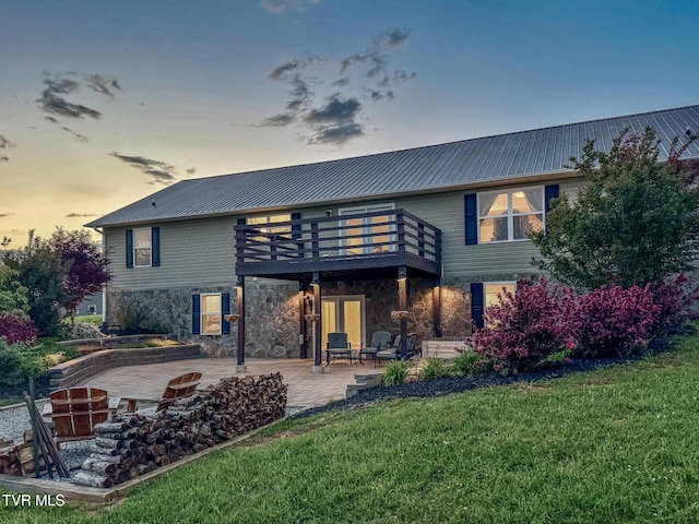 back of house featuring stone siding, a yard, a patio, metal roof, and a wooden deck