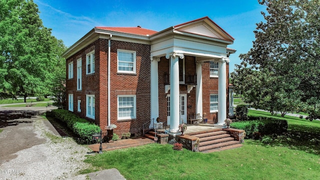 greek revival inspired property with a front yard, metal roof, and brick siding