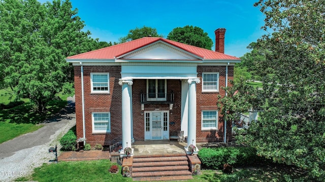greek revival house featuring a chimney, metal roof, and brick siding