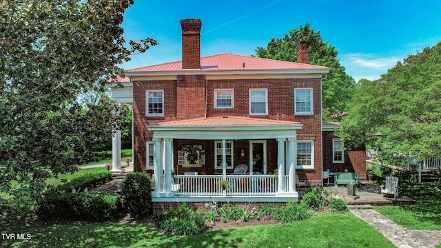 back of house with brick siding, a chimney, and metal roof
