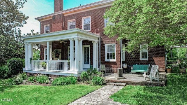 view of front of property with covered porch, brick siding, a chimney, and a front lawn