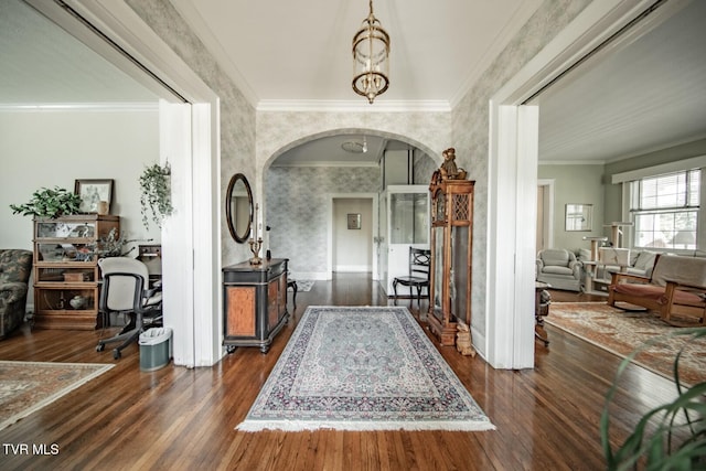 entryway featuring crown molding, arched walkways, wallpapered walls, and dark wood-type flooring