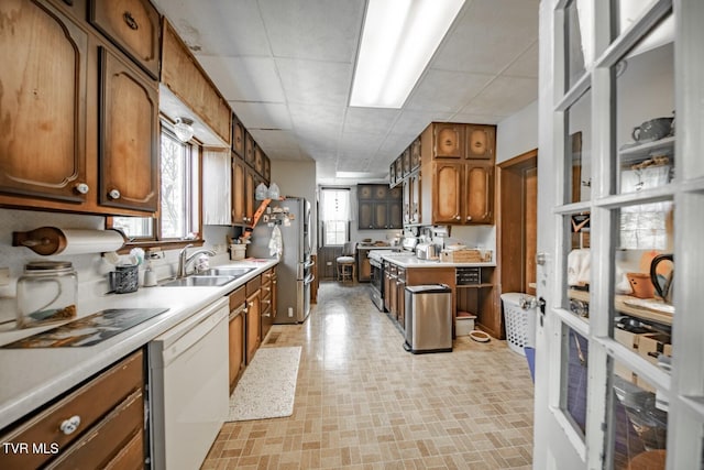 kitchen with brown cabinets, appliances with stainless steel finishes, a sink, light countertops, and a drop ceiling