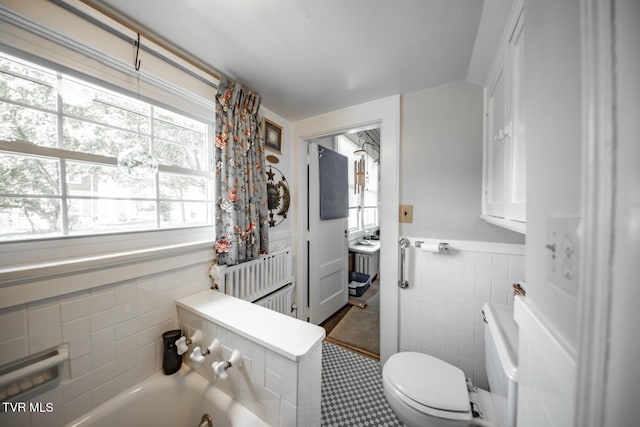 bathroom with a healthy amount of sunlight, tile walls, a washtub, and toilet