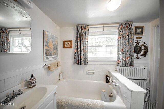 bathroom featuring a healthy amount of sunlight, radiator heating unit, a tub with jets, and tile walls