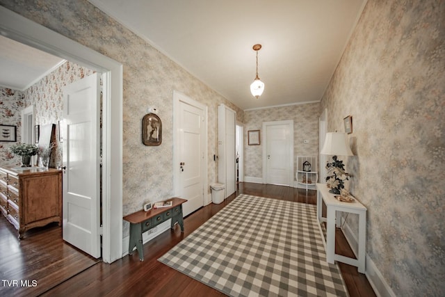 entryway featuring dark wood-type flooring, ornamental molding, baseboards, and wallpapered walls