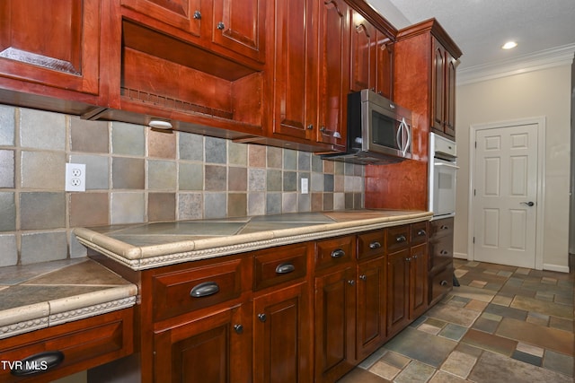 kitchen with backsplash, white oven, light countertops, stainless steel microwave, and ornamental molding