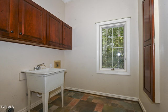 washroom featuring washer hookup, baseboards, stone finish floor, and cabinet space