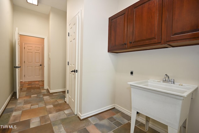 laundry room featuring electric dryer hookup, stone finish flooring, cabinet space, a sink, and baseboards