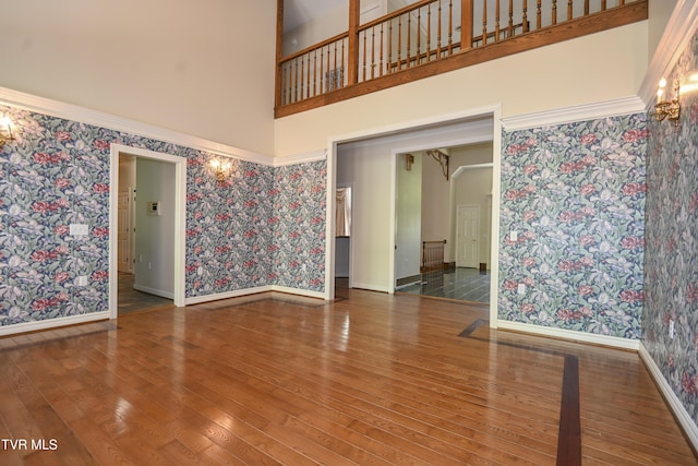 spare room with wood-type flooring, baseboards, a high ceiling, and wallpapered walls