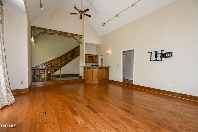 unfurnished living room with stairway, high vaulted ceiling, a ceiling fan, and wood finished floors