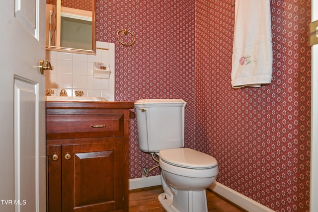 half bathroom featuring baseboards, toilet, wallpapered walls, and wood finished floors