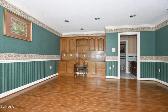 empty room featuring wood-type flooring, ornamental molding, and a wainscoted wall