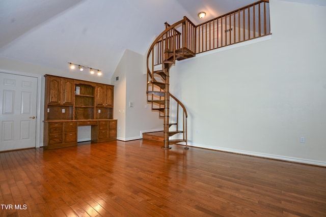 unfurnished living room featuring track lighting, stairs, hardwood / wood-style floors, baseboards, and high vaulted ceiling