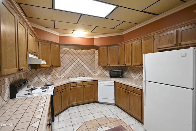 kitchen with white appliances, tile countertops, under cabinet range hood, and decorative backsplash