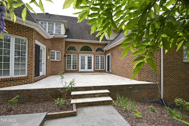 doorway to property featuring brick siding, french doors, a shingled roof, and a patio area
