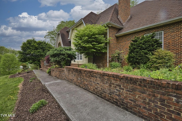 view of side of home with brick siding, a chimney, and roof with shingles